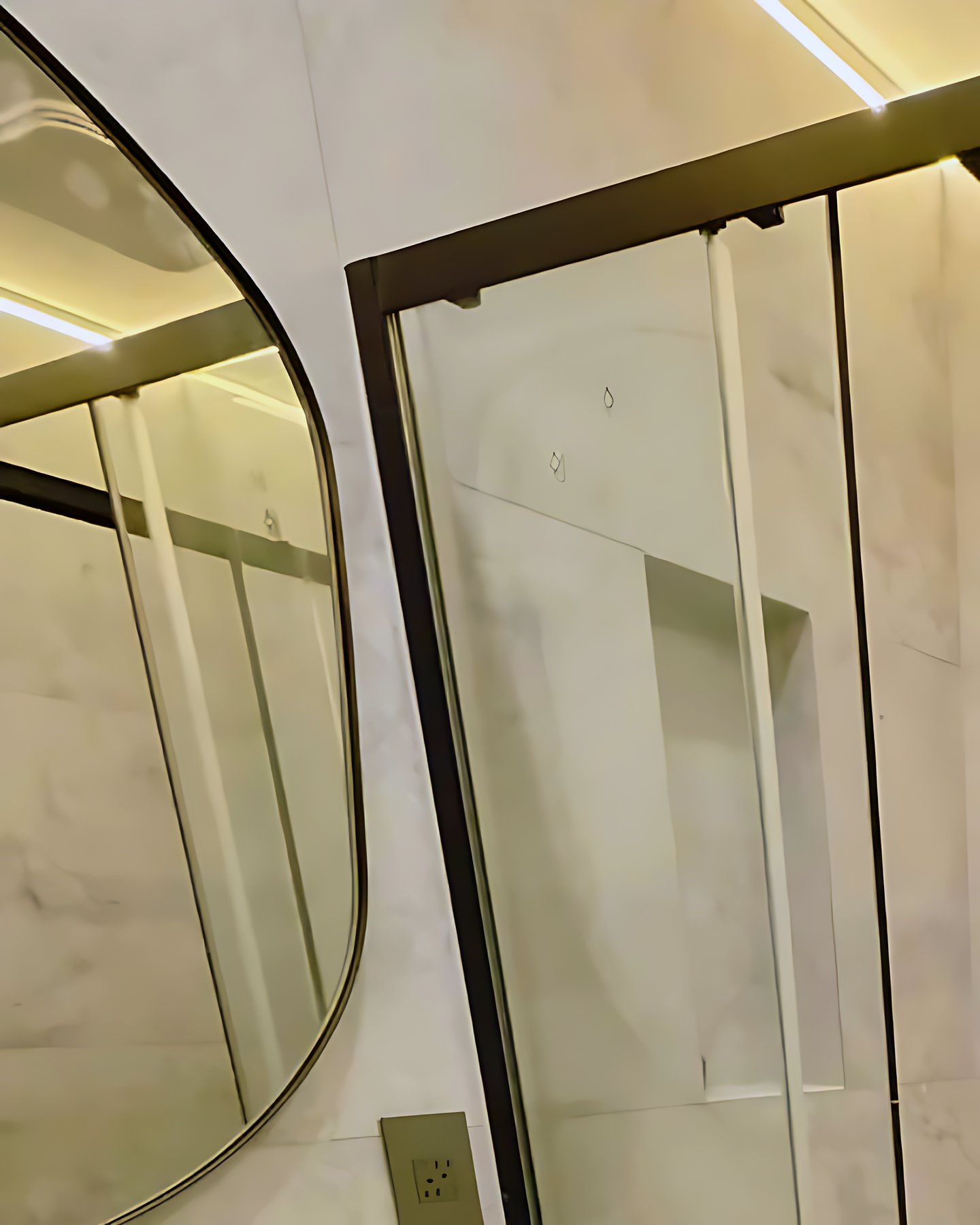 Glass shower beside a backlit vanity mirror